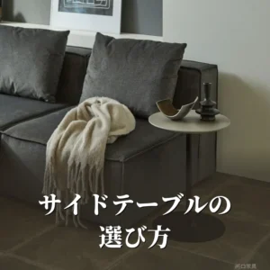 グレーのソファの横に置いたCielサイドテーブル。丸い天板の上にオブジェと花瓶をのせ、黒い一本脚で立っている