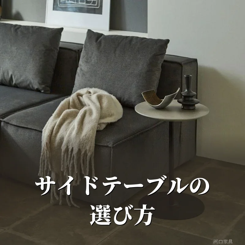 グレーのソファの横に置いたCielサイドテーブル。丸い天板の上にオブジェと花瓶をのせ、黒い一本脚で立っている